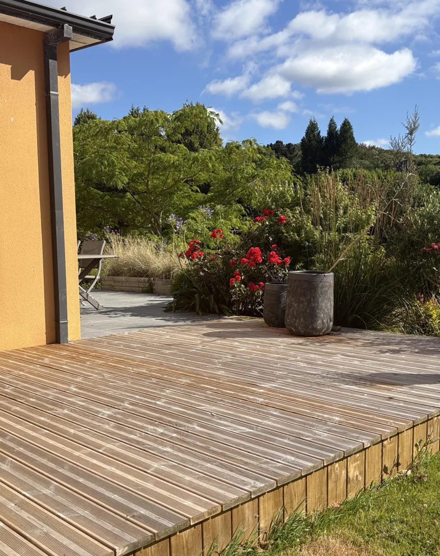 Terrasse bois devant un jardin paysager sous un ciel bleu
